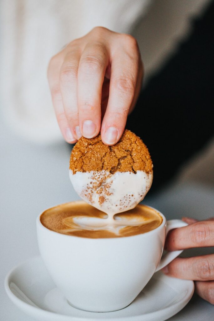 person holding white ceramic mug with brown and white liquid